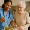 Caregiver in medical scrubs helping a senior woman prepare a salad in a Houston home kitchen as part of in-home health care services.